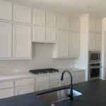 Modern kitchen featuring white cabinetry, a sleek black countertop, and stainless steel appliances, showcasing The Perfect Cabinet Company's custom cabinetry and remodeling services.
