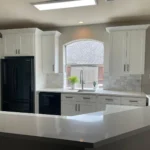 Modern kitchen with white cabinetry, black appliances, and a large island, showcasing custom cabinetry and remodeling services by The Perfect Cabinet Company.