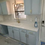 Kitchen countertop with light blue cabinetry, modern faucet, and a window reflecting remodeling work, showcasing The Perfect Cabinet Company's kitchen remodeling services.