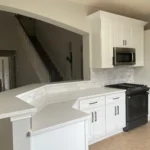 Modern kitchen featuring white cabinetry, quartz countertops, stainless steel appliances, and an open layout with a view of a staircase.