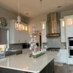 Modern kitchen interior featuring sleek cabinetry, a large island with a decorative centerpiece, stainless steel appliances, and stylish pendant lighting, showcasing The Perfect Cabinet Company's remodeling expertise.