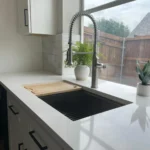 Modern kitchen sink with sleek faucet, white countertop, cutting board, and plants, showcasing custom cabinetry and remodeling features by The Perfect Cabinet Company.
