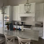 Modern kitchen interior with white cabinetry, marble countertop, pendant lighting, and a central island, showcasing The Perfect Cabinet's custom cabinetry and remodeling expertise.