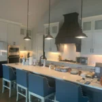 Modern kitchen featuring a spacious island with blue seating, sleek cabinetry, and a stylish range hood, showcasing The Perfect Cabinet Company's remodeling expertise.