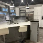 Modern kitchen design featuring a sleek island with white bar stools, gray cabinetry, stainless steel appliances, and stylish lighting, showcasing The Perfect Cabinet Company's remodeling expertise.