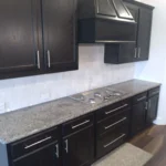 Modern kitchen featuring sleek black cabinetry, a granite countertop, and a stainless steel range hood, showcasing The Perfect Cabinet Company's custom cabinetry and remodeling services.