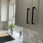 Modern kitchen cabinetry with sleek black handles, stainless steel sink, and natural light from window, showcasing The Perfect Cabinet's custom cabinetry and kitchen remodeling services.