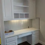 White cabinetry with a built-in desk and shelves, featuring under-cabinet lighting, in a modern kitchen setting, highlighting custom cabinetry and remodeling services.