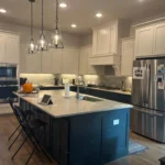 Modern kitchen featuring a large island with seating, white cabinetry, stainless steel appliances, and pendant lighting, showcasing The Perfect Cabinet Company's custom cabinetry and kitchen remodeling services.