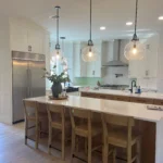 Modern kitchen with custom cabinetry, large island, pendant lighting, and stainless steel appliances, showcasing The Perfect Cabinet's remodeling services.