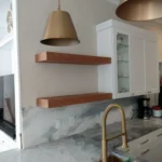 Modern kitchen design featuring white cabinetry, wooden open shelves, a gold pendant light, and a marble countertop, showcasing The Perfect Cabinet's custom cabinetry and remodeling expertise.