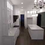 Modern kitchen interior featuring white cabinetry, an island, and elegant lighting fixtures, highlighting The Perfect Cabinet Company's custom cabinetry and remodeling services.