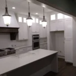 Modern kitchen with white cabinetry, pendant lighting, stainless steel appliances, and a large island, showcasing The Perfect Cabinet's remodeling expertise.