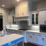 Modern kitchen design featuring white cabinetry, a central island with a blue base, and stainless steel appliances, showcasing The Perfect Cabinet Company's custom cabinetry and remodeling expertise.