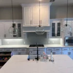 Modern kitchen with white cabinetry, pendant lighting, and a central island, showcasing custom cabinetry and remodeling features.