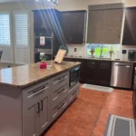 Modern kitchen interior featuring dark cabinetry, granite countertops, stainless steel appliances, and natural light from windows, showcasing The Perfect Cabinet Company's remodeling expertise.