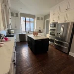 Modern kitchen featuring custom cabinetry, an island with a dark finish, stainless steel appliances, and large windows providing natural light.