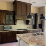Modern kitchen featuring dark wood cabinetry, granite countertops, stainless steel appliances, and pendant lighting, showcasing The Perfect Cabinet Company's custom cabinetry and remodeling expertise.