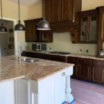 Modern kitchen design featuring dark wooden cabinetry, granite countertops, and pendant lighting over an island, showcasing remodeling services by The Perfect Cabinet Company.