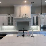 Modern kitchen design featuring white cabinetry, pendant lighting, and a large island with a sleek countertop, showcasing The Perfect Cabinet Company's remodeling services.