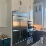 Modern kitchen with stainless steel refrigerator, built-in oven, and custom cabinetry, showcasing The Perfect Cabinet's remodeling services.