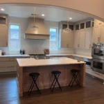 Modern kitchen design featuring an island with seating, light wood cabinetry, stainless steel appliances, and large windows for natural light.