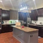 Modern kitchen featuring dark wooden cabinets, granite island countertop, and contemporary lighting, showcasing The Perfect Cabinet's custom cabinetry and remodeling services.