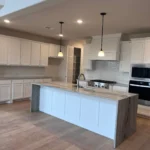 Modern kitchen featuring white cabinetry, an island with a light countertop, stainless steel appliances, and pendant lighting, showcasing The Perfect Cabinet's custom cabinetry and remodeling services.