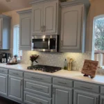 Modern kitchen with gray cabinetry, stainless steel appliances, and a light countertop, featuring a gas stove and decorative elements, showcasing custom cabinet design by The Perfect Cabinet Company.
