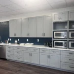 Modern kitchen design featuring gray cabinetry, white countertops, and multiple built-in microwaves against a dark blue wall, showcasing The Perfect Cabinet's remodeling expertise.
