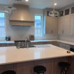 Modern kitchen with white cabinetry, large island, stainless steel appliances, and pendant lighting, showcasing custom cabinetry and remodeling services by The Perfect Cabinet Company.