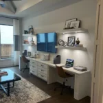 Modern office setup with white cabinetry, dual workstations, decorative shelves, and natural light, showcasing The Perfect Cabinet's design capabilities.