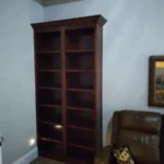Dark wood bookshelf with multiple shelves, positioned in a corner of an office space, complementing the cabinetry and interior design themes of The Perfect Cabinet.