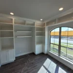 Office space showcasing custom cabinetry with built-in shelves and large window, designed for functionality and natural light.