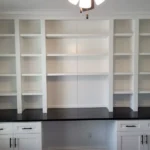 Modern white cabinetry with open shelves and a dark countertop, showcasing custom cabinetry design for office spaces.