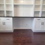 Modern white cabinetry with open shelves and dark countertop in an office setting, showcasing The Perfect Cabinet's design and remodeling services.