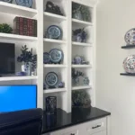 Office cabinetry featuring white shelves displaying decorative plates and plants, with a black countertop and a computer monitor, showcasing The Perfect Cabinet's design and remodeling capabilities.
