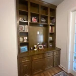 Wooden cabinetry with shelves and drawers, showcasing decorative items and books, in an office setting, highlighting The Perfect Cabinet's custom cabinetry solutions.