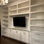 Modern white cabinetry with built-in shelves and a television, showcasing custom design for office and home remodeling.