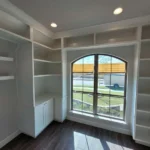 Office space featuring custom cabinetry and built-in shelves, large arched window providing natural light, designed for functionality and aesthetics.
