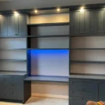 Custom cabinetry with dark wood finish and integrated lighting, featuring open shelves and a blue backlit section, showcased in The Perfect Cabinet's office photo gallery.