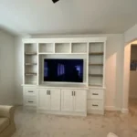 Modern white cabinetry with built-in shelving and TV unit in a cozy office setting.