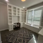 Office space featuring custom cabinetry, built-in shelves, a desk, and natural light from large windows, showcasing The Perfect Cabinet's design capabilities.