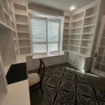Office space featuring white cabinetry, built-in shelves, and a cozy chair, showcasing The Perfect Cabinet's design capabilities for remodeling projects.