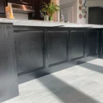 Custom black kitchen island cabinetry with sleek paneling, showcasing modern design elements, in a well-lit kitchen setting.
