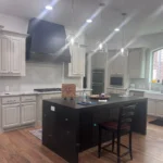 Custom kitchen island with black countertop, white cabinetry, modern lighting, and wood flooring, showcasing The Perfect Cabinet's design style.