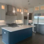 Custom kitchen island with blue cabinetry, white countertop, modern appliances, and pendant lighting in a bright kitchen setting.