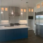Modern kitchen featuring a custom blue island with a white countertop, stainless steel appliances, and stylish pendant lighting, showcasing cabinetry by The Perfect Cabinet.