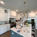 Custom kitchen island with white cabinetry and dark blue base, modern pendant lighting, and kitchen appliances, showcasing functional design and stylish decor.