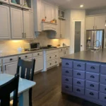 Custom kitchen island with purple cabinetry and storage drawers, surrounded by light gray cabinets and modern appliances, showcasing a stylish kitchen design by The Perfect Cabinet.